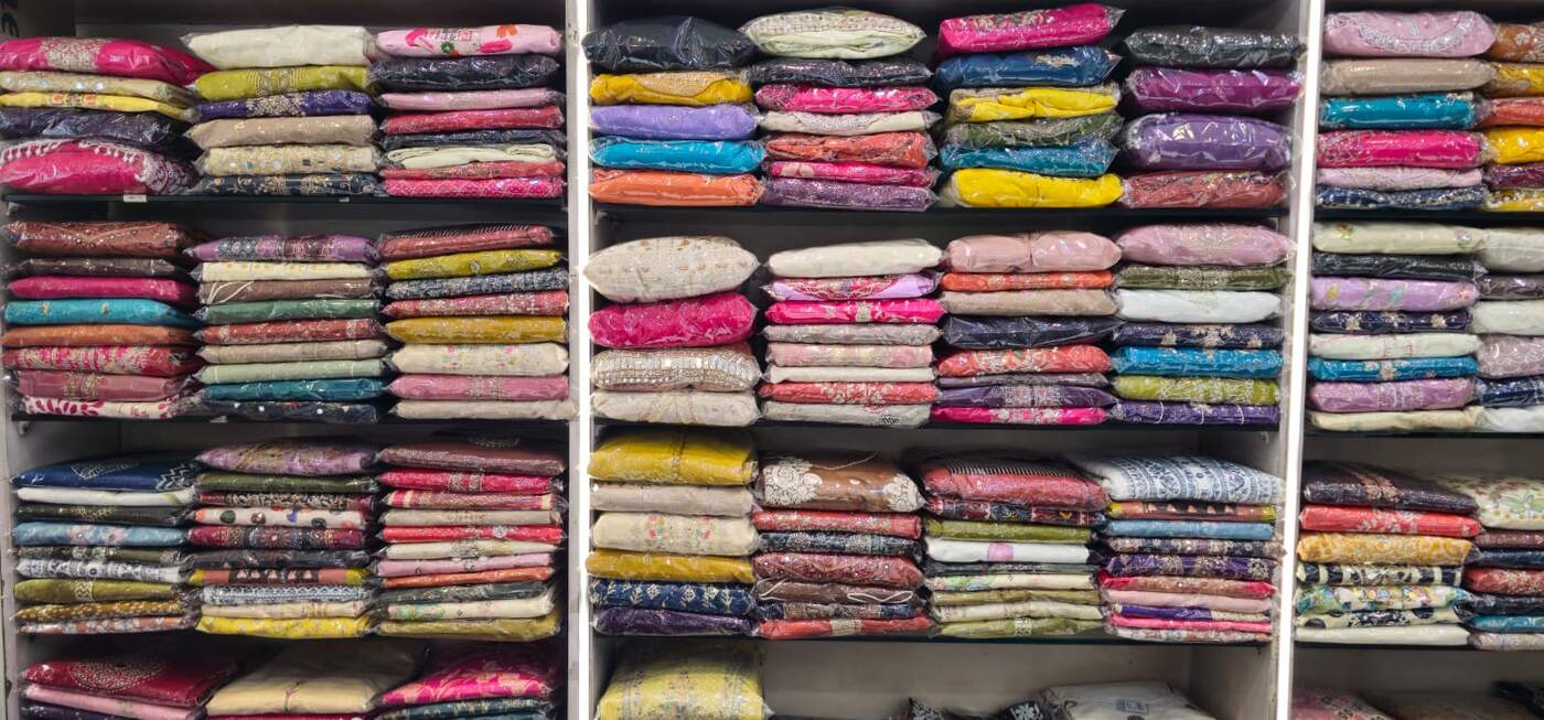 Shelves stacked with folded fabric bundles in every colour at Radha Fashion